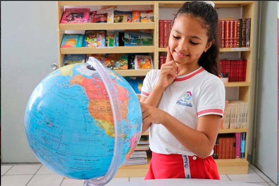 Aluna com globo terrestre diante da estante de livros
